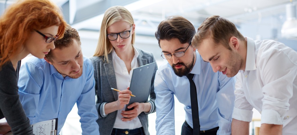 チームメンバーが、テーブルの上に広げられた書類を通じてプロジェクトの詳細を活発に議論し、チームワークとコミュニケーションを促進している。