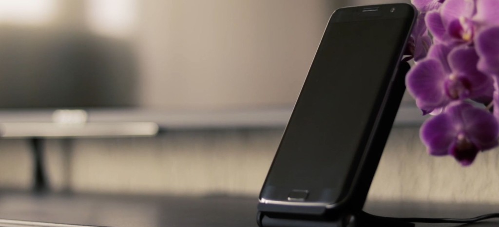 黒いスマートフォンがスタンドに立てかけられ、背景には紫の花が置かれています。シンプルなデザインで、モダンな雰囲気を醸し出しています。
