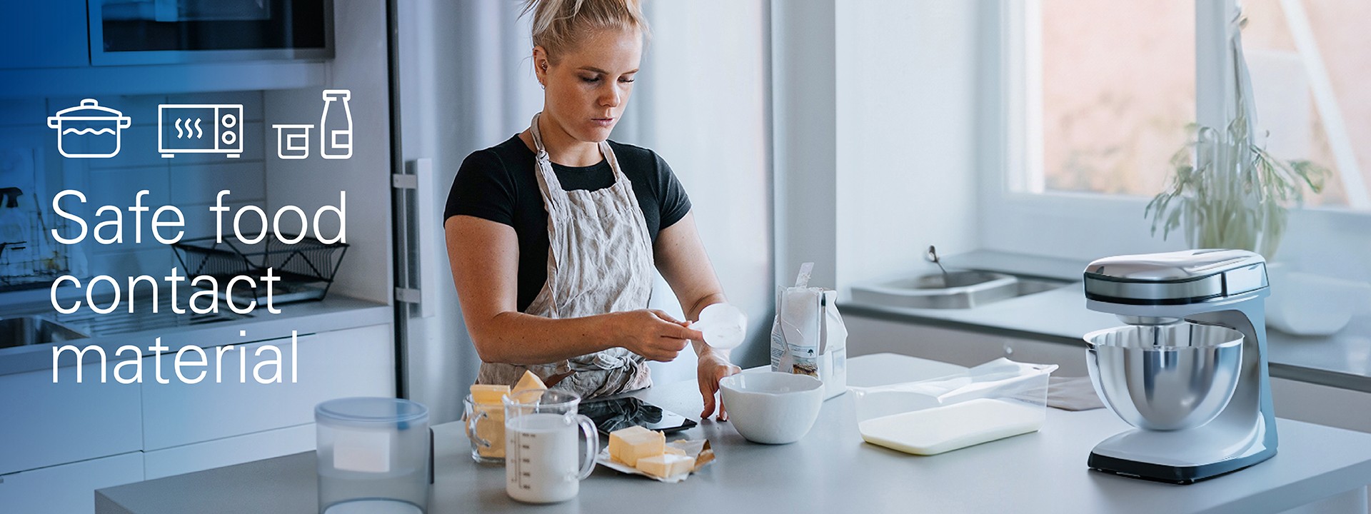 Young woman baking in her kitchen, the work surface covered with a variety of housewares, household appliances and food packaging