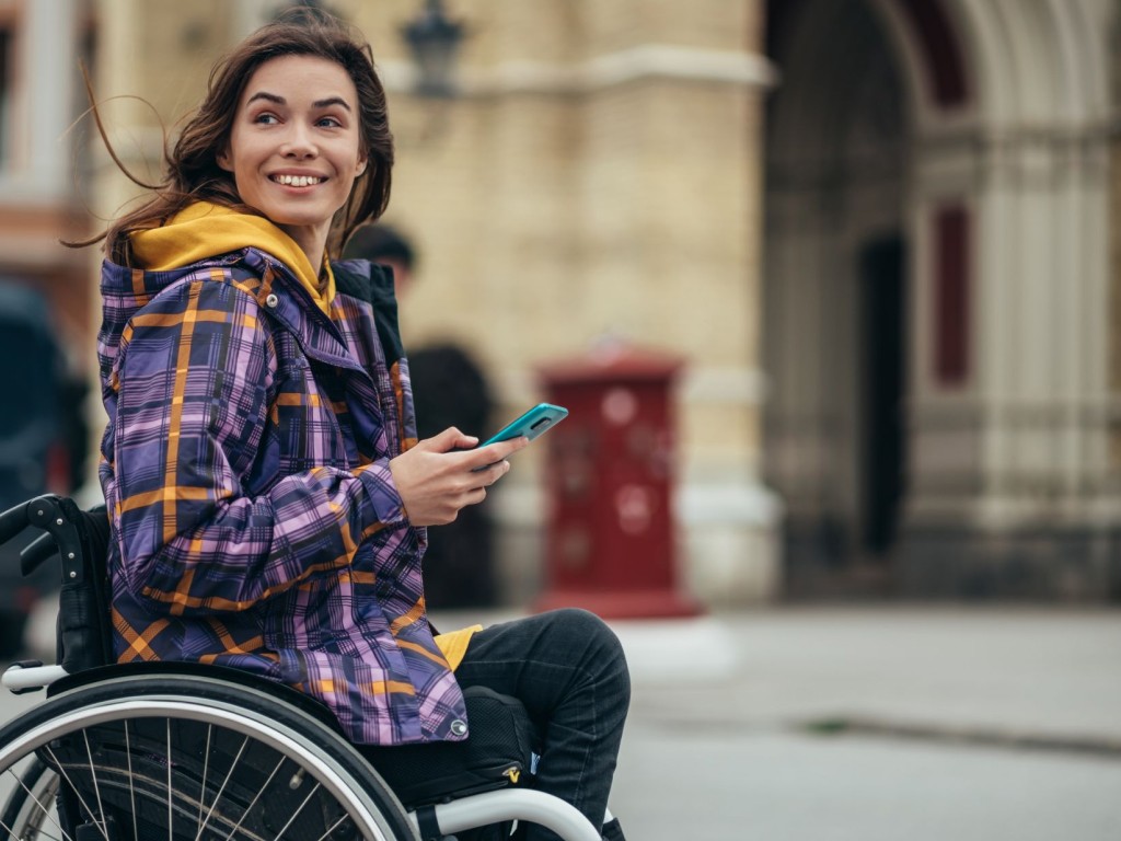 Frau im Rollstuhl mit Smartphone in der Hand.