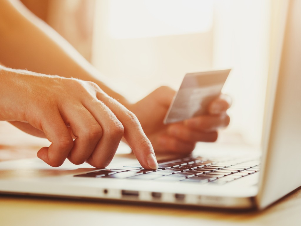 Zwei Hände auf Computer-Tastatur, eine davon hält eine Kreditkarte. 