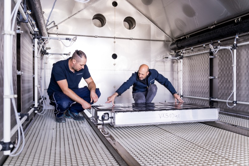 Two technicians positioning a large battery module inside a testing chamber