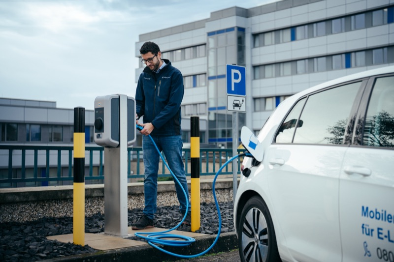 Man connecting a charging cable to an electric vehicle at a charging station