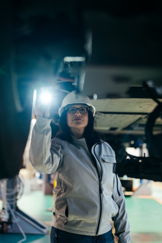 Female inspector in a hard hat and work jacket using a flashlight to examine industrial equipment